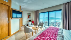 A hotel room with a large bed, a TV, a desk with chairs, and a view of the ocean. - Azalai Hotel Dakar (Dakar)