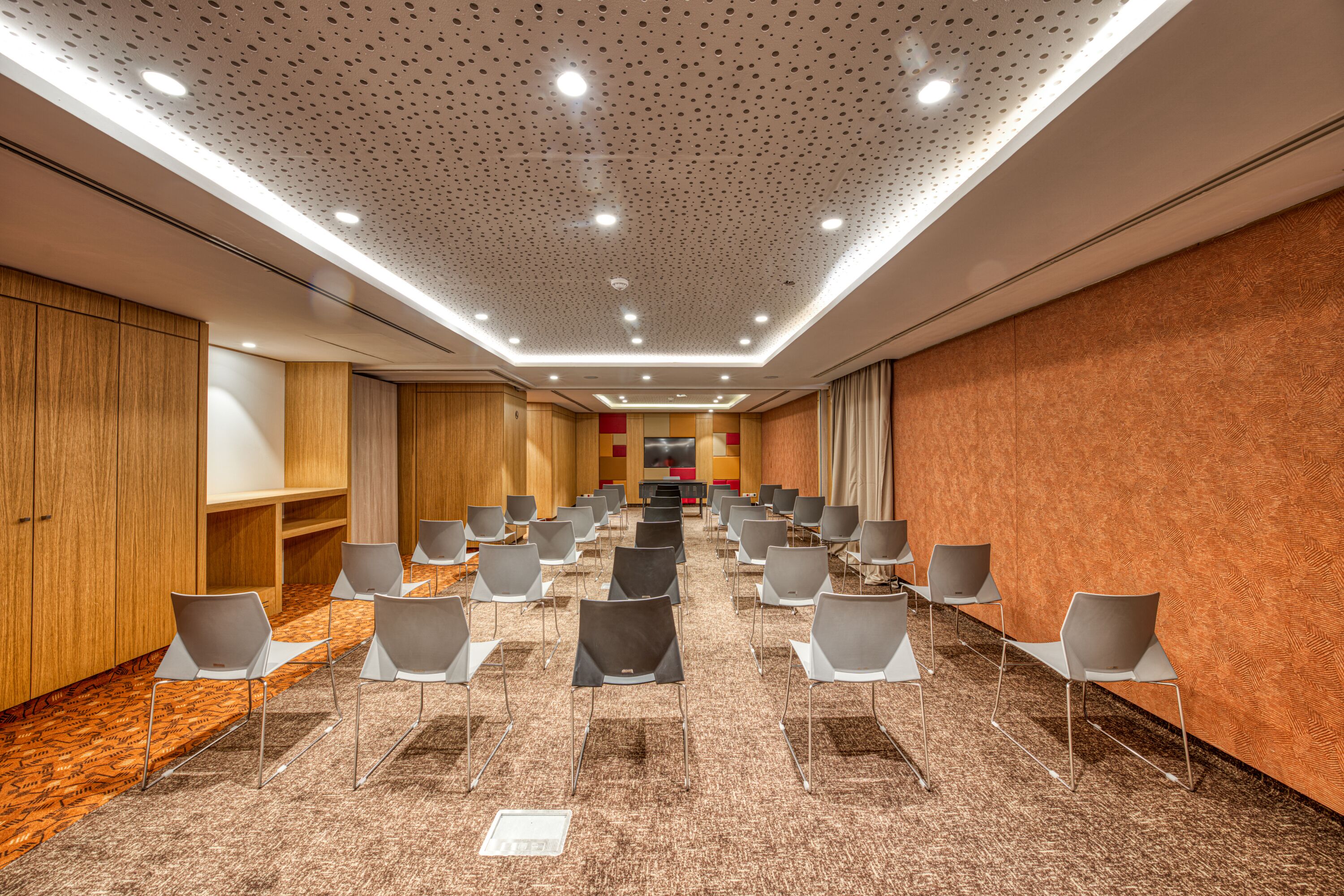 Un salón de conferencias con filas de sillas, un panel de pared de madera y una alfombra estampada.