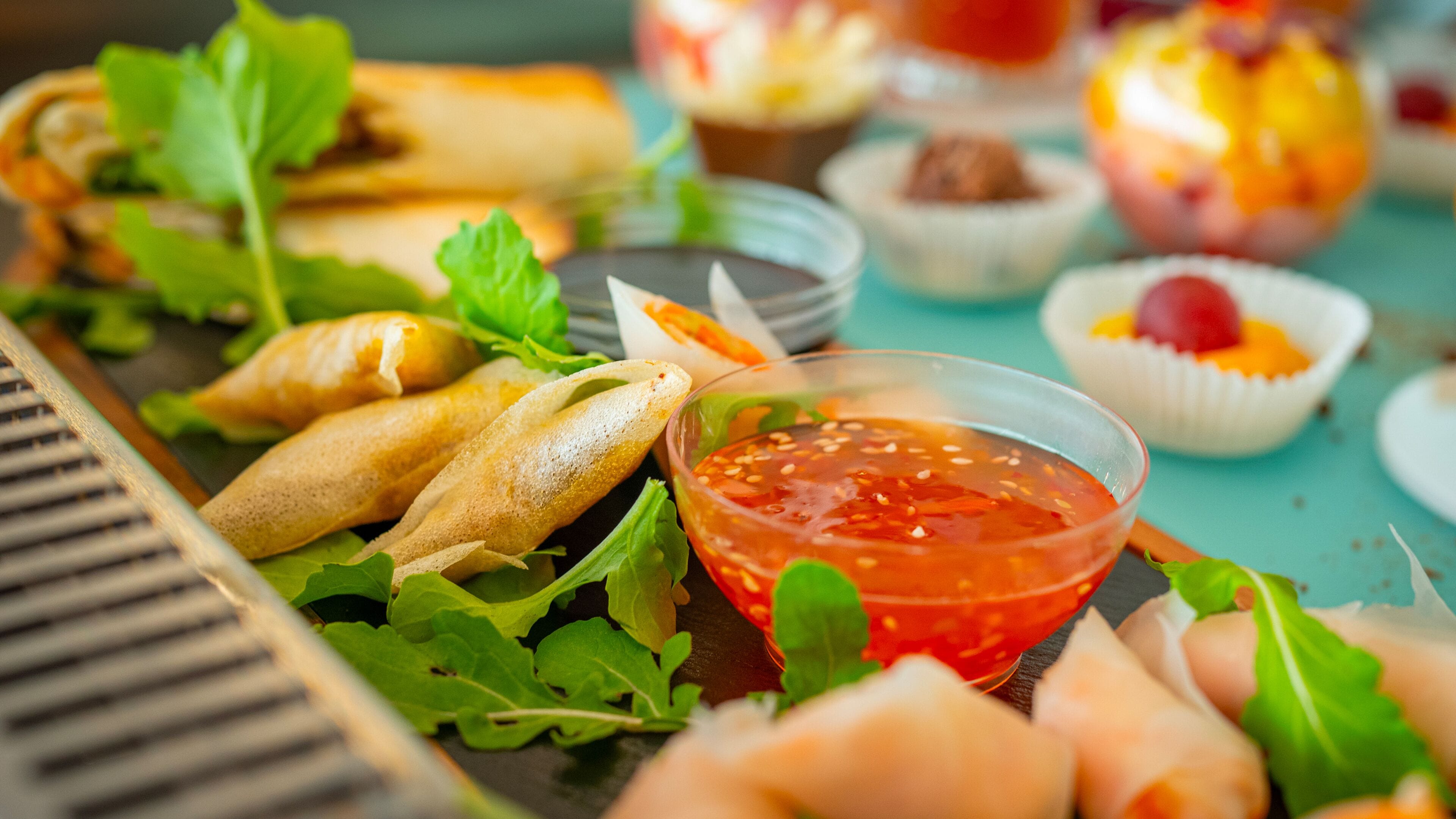 A variety of appetizers including spring rolls, fresh greens, and a bowl of red dipping sauce on a table.
