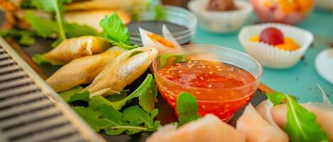 A variety of appetizers including spring rolls, fresh greens, and a bowl of red dipping sauce on a table.