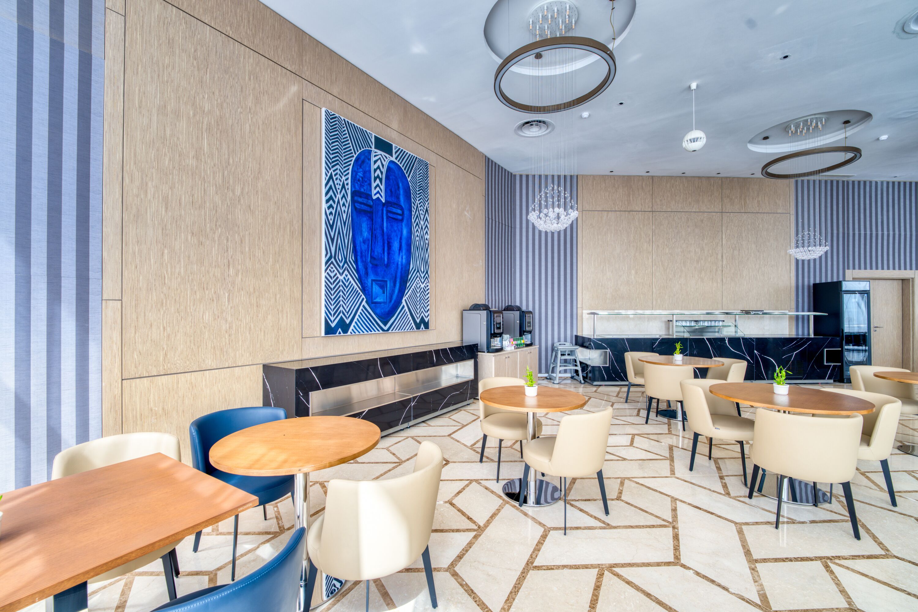 Un moderno hall de hotel con mesas redondas, sillas, un gran cuadro abstracto, una zona de bar y un suelo con estampado.