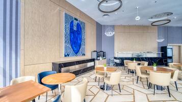 Un moderno hall de hotel con mesas redondas, sillas, un gran cuadro abstracto, una zona de bar y un suelo con estampado.