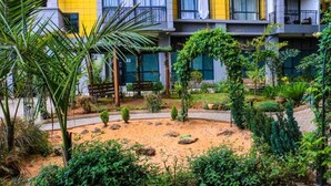 A courtyard with a sandy area, various plants, and a building with balconies.