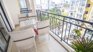 A balcony with wicker furniture, a potted plant, and a city view.