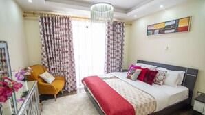 A bedroom with a bed, a chair, a desk, and a window with curtains.