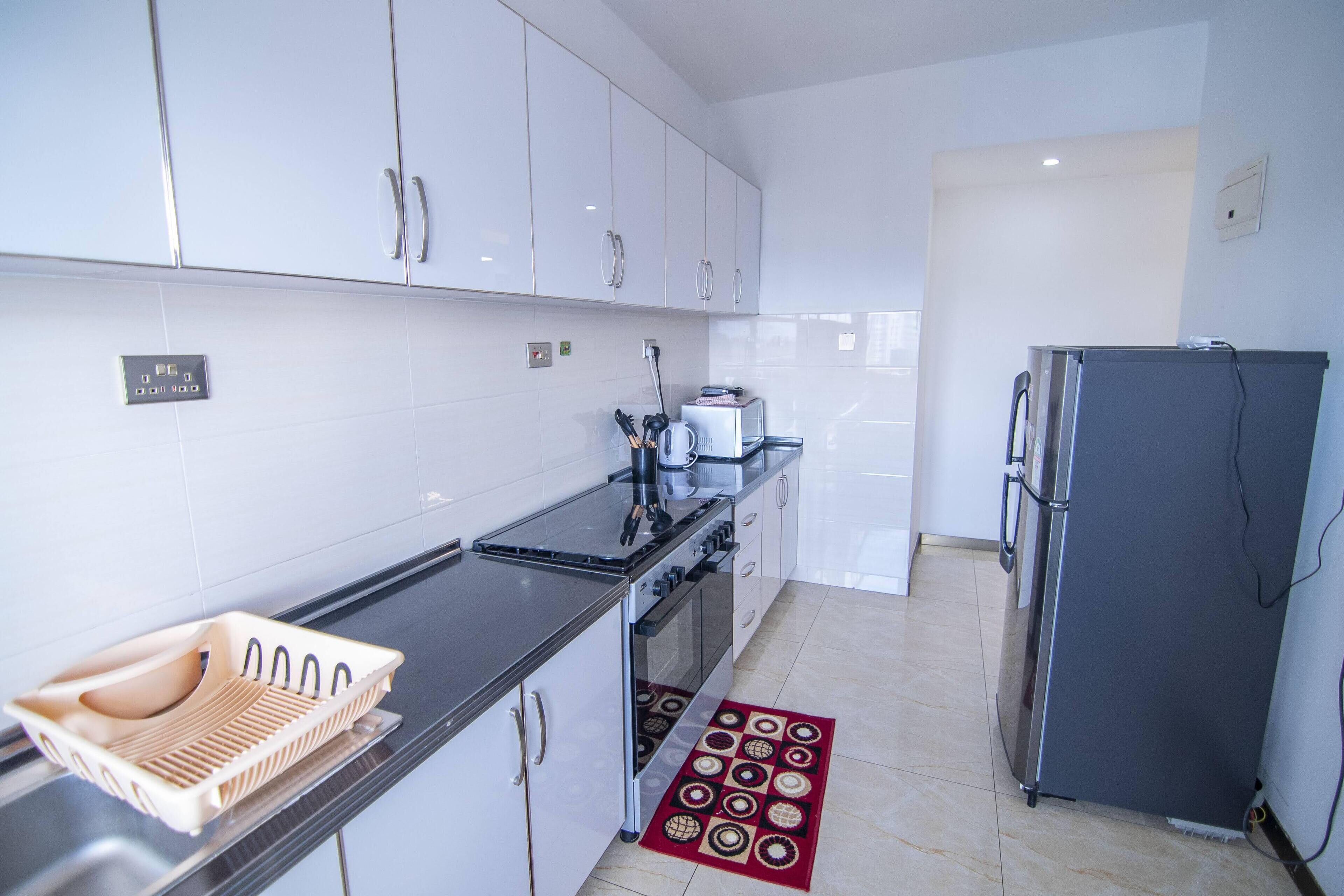 A modern kitchen with white cabinets, a black countertop, a stainless steel refrigerator, and a red patterned rug.