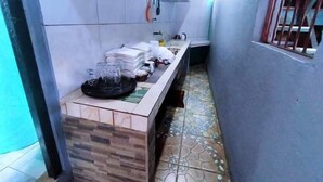 A narrow corridor with a kitchen area on one side, featuring a counter with stacked plates and glasses, and a tiled floor. - Maritonies Place (Coron)