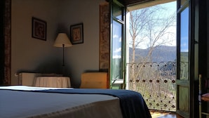 Ein Schlafzimmer mit einem Bett, einem Nachttisch, einer Lampe und einem Fenster mit Blick auf Bäume und Berge.
