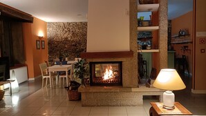 Ein gemütliches Wohnzimmer mit Kamin, Essbereich und Küchenzeile mit Regalen.
