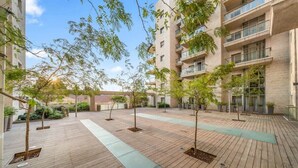 A courtyard with wooden flooring, potted trees, and a building with multiple balconies. - Luxurious 1BDR Terrace Parking in City Central (Jerusalem)