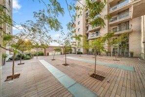 Un patio con piso de madera, árboles en macetas y un edificio con varios balcones.