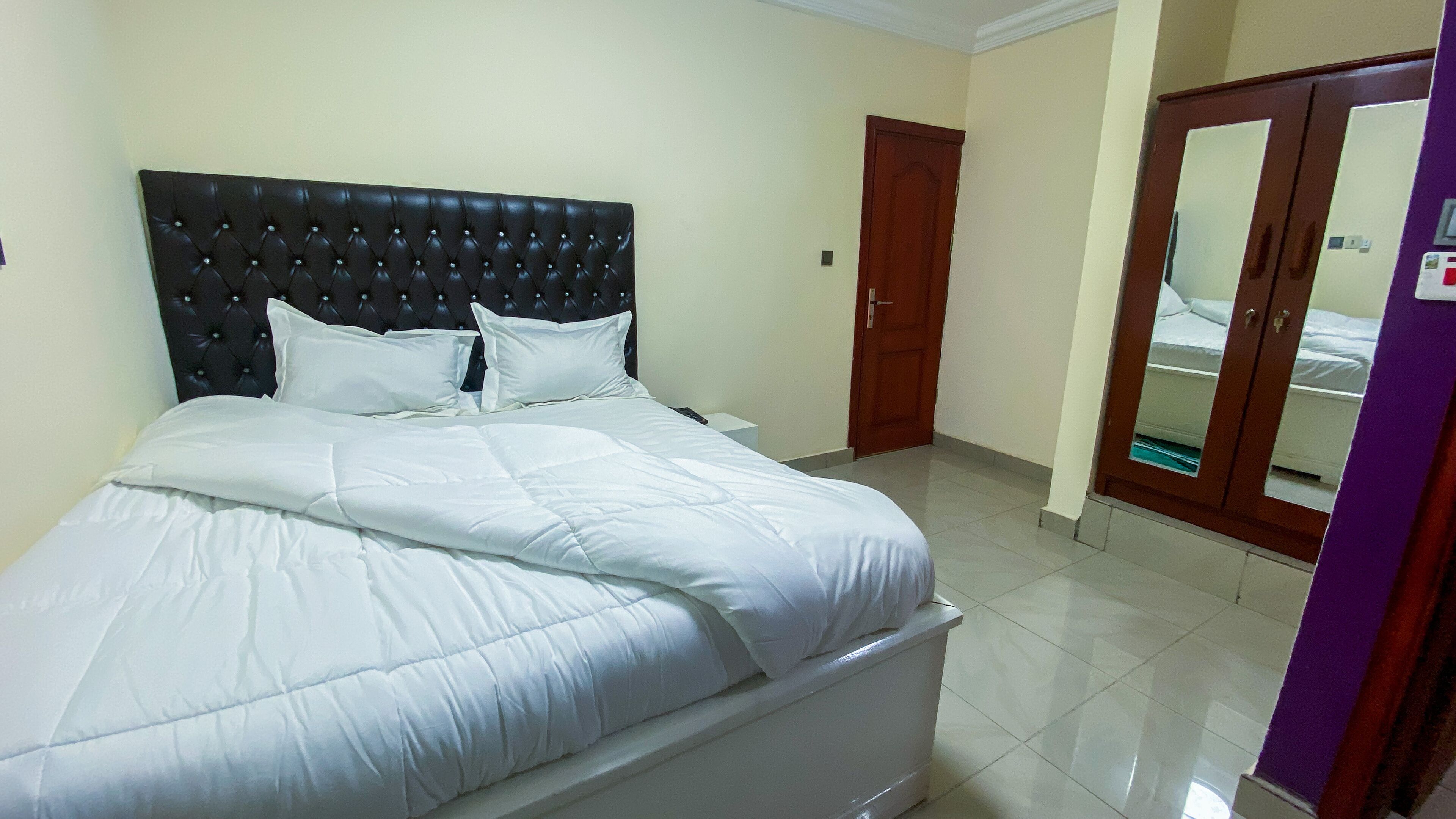A neatly made bed with a tufted headboard, a bedside table, and a door leading to another room.