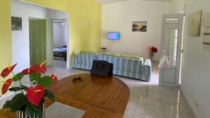 Una habitación con piso de madera, una cama con ropa de cama a rayas, un televisor en la pared y una puerta con espejo.