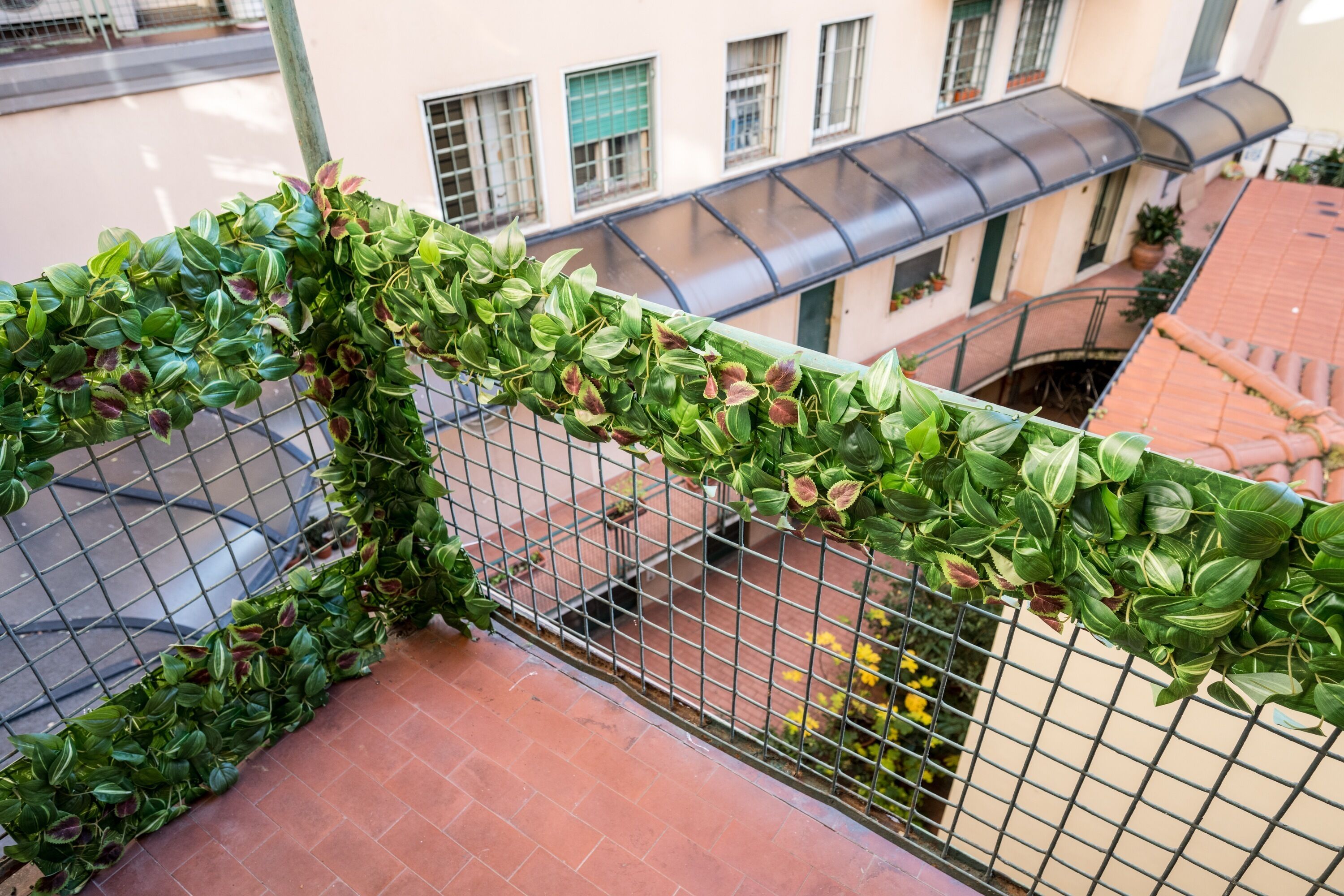 A balcony with a metal railing, green foliage, and a view of a building with windows and a tiled roof.