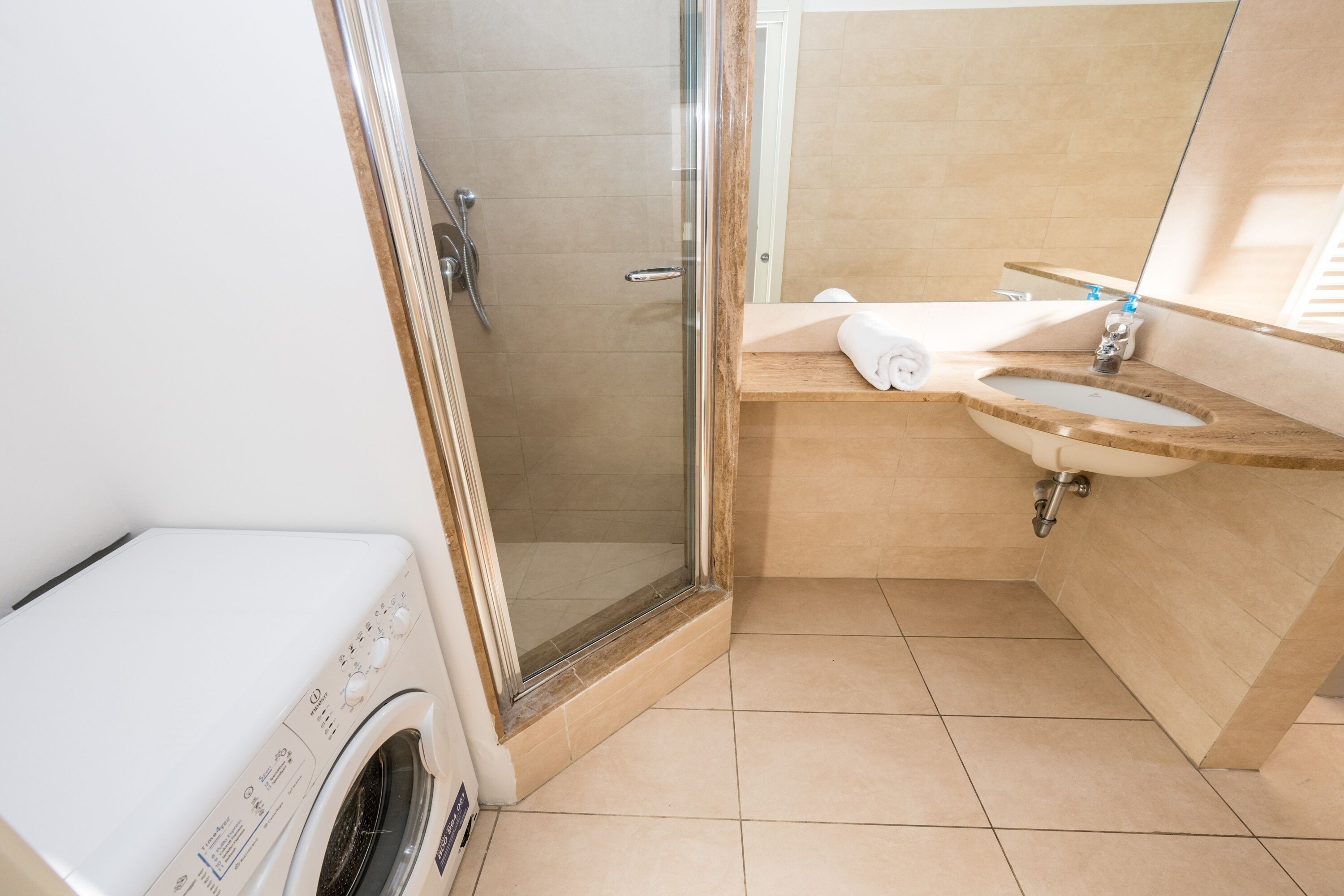 Een moderne badkamer met een douche met glazen wand, een inbouw wasmachine en een wastafel met spiegel erboven.