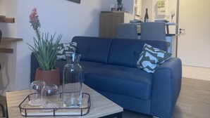 Una sala de estar con un sofá azul, una mesa de centro con adornos, una planta en maceta y un cuadro en la pared.