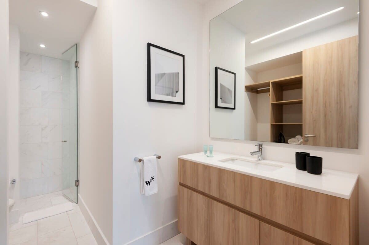 Een moderne badkamer met een glazen douche, een houten wastafelmeubel en een grote spiegel.