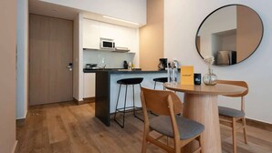 A modern kitchen with white cabinets, a microwave, and a coffee machine. There is a round mirror on the wall, a small table with two chairs, and a door leading to another room. - w* | Stunning loft in Cuauhtemoc (Ciudad de México)