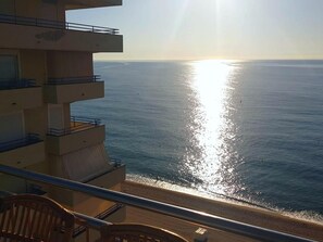 Un balcón con vista al mar y el sol reflejándose en el agua.