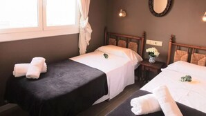 Ein Hotelzimmer mit zwei Betten, einem Vorhangfenster, einem Nachttisch mit Blumenvase und einem an der Wand befestigten Spiegel.