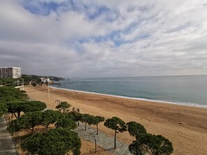 A beach with a paved walkway, trees, and a building in the background.