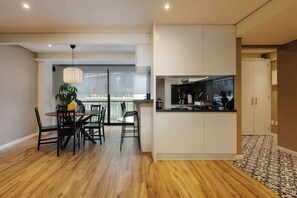 Une cuisine moderne avec des meubles blancs, un plan de travail noir et un coin repas comprenant une table et des chaises en bois.