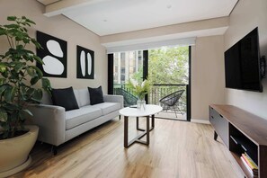 Un salon moderne avec un canapé gris, une table basse ronde et un téléviseur fixé au mur.