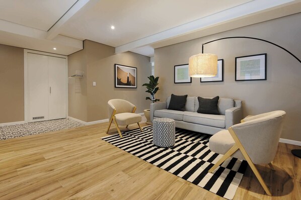 Un salon moderne avec un canapé, des fauteuils, un tapis à motifs et des œuvres d’art accrochées au mur.