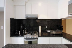 Una cocina moderna con armarios blancos, una estufa a gas, una cafetera y un lavamanos.