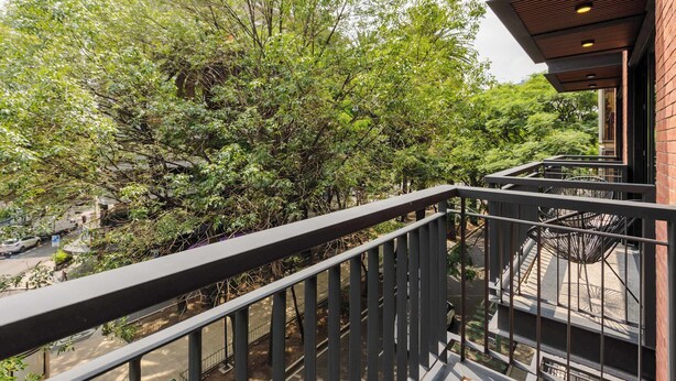 Un balcone con ringhiera in metallo che si affaccia su un giardino con diversi alberi e arbusti.
