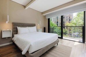 Une chambre moderne avec un grand lit, des tables de chevet et une vue sur la ville depuis un balcon.