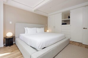 Un dormitorio con una cama grande, una mesita de noche, un armario y una pequeña mesa redonda con una lámpara.