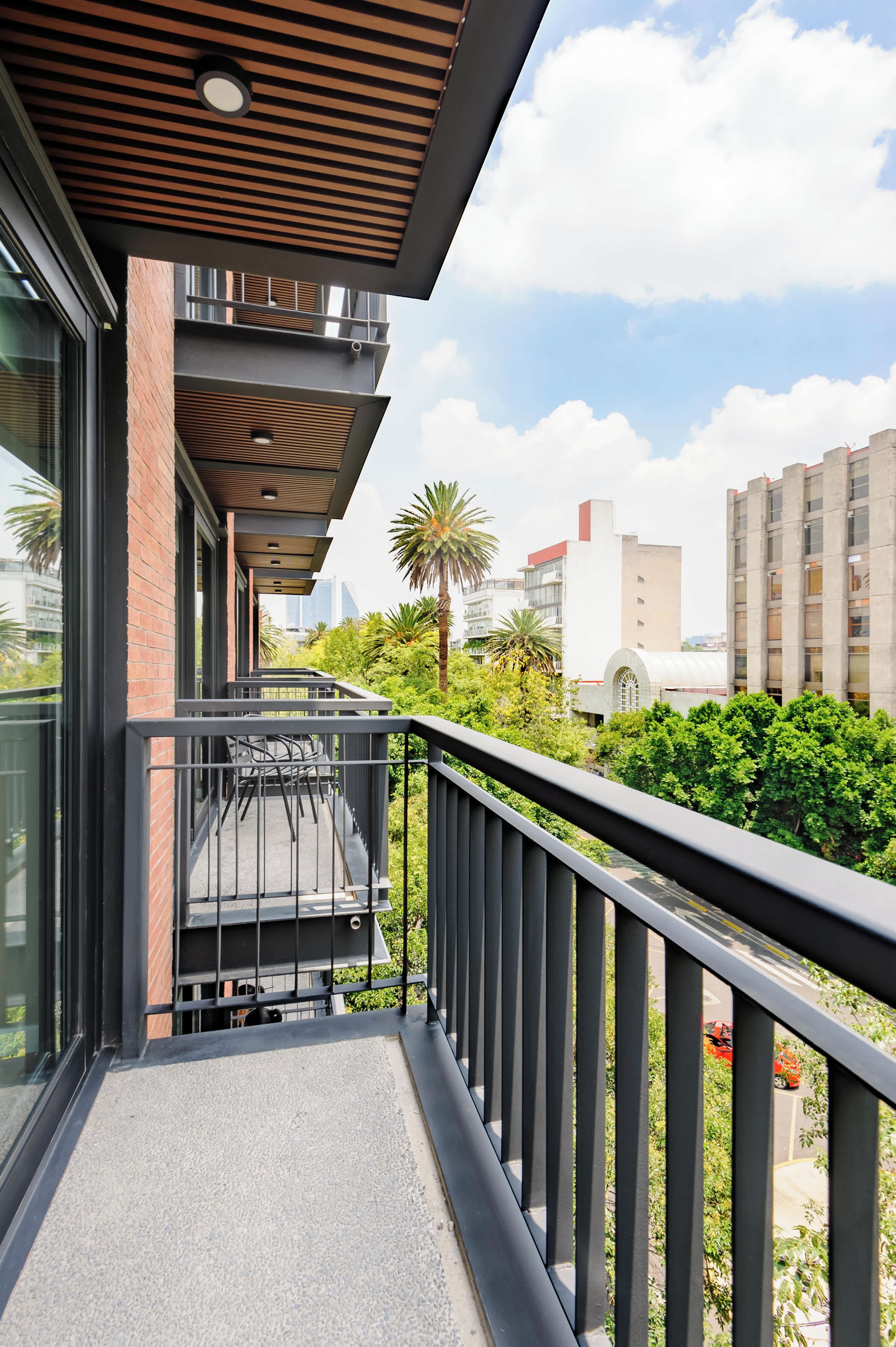 Ein Balkon mit Blick auf eine Stadtlandschaft, eine Palme und ein Gebäude mit rotem Dach.