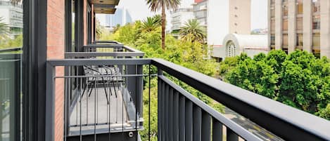 A balcony with a view of a cityscape, a palm tree, and a building with a red roof.