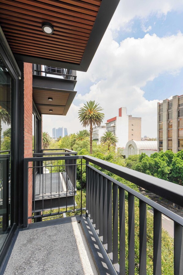 A balcony with a metal railing, a wooden ceiling, and a view of a cityscape with buildings and palm trees.