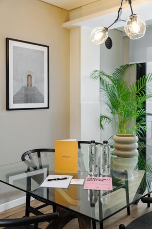A modern interior with a glass table, chairs, a framed artwork, a potted plant, and a welcome sign.