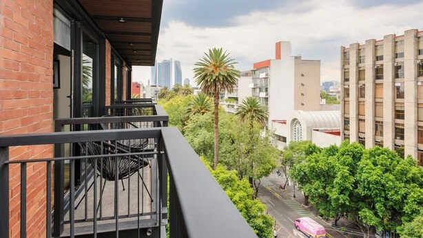 A balcony with a view of a cityscape, including buildings and palm trees. - w* | Vibrant 2BR with Balcony in Condesa (Ciudad de México)