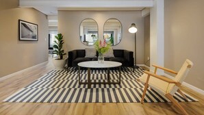 A modern living room with a round coffee table, a sofa, and a chair. There are two large mirrors on the wall, a floor lamp, and a potted plant. - w* | Vibrant 2BR with Balcony in Condesa (Ciudad de México)