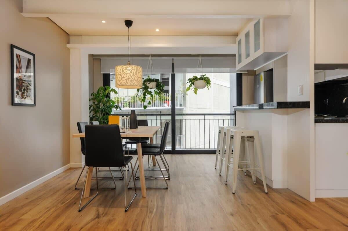 A modern kitchen with a dining area, wooden flooring, hanging plants, and a view to the outside. - w* | Vibrant 2BR with Balcony in Condesa (Ciudad de México)