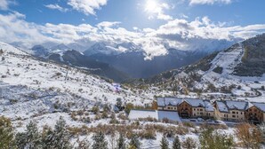 Eine verschneite Berglandschaft mit einer Berghütte, mehreren Gebäuden und einer Seilbahn.