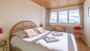 Ein Schlafzimmer mit Holzbalkendecke, einem Bett mit weißer Bettwäsche, einem Fenster mit Blick auf den Himmel und einem roten Sessel.