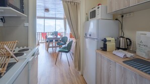 Eine kompakte Küche mit Mikrowelle, Wasserkocher und kleinem Kühlschrank. Ein Essbereich mit Tisch und Stühlen lädt zum Verweilen ein, und durch ein Fenster eröffnet sich eine Aussicht.