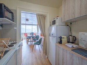 A compact kitchen with a microwave, kettle, and a small refrigerator. There's a dining area with a table and chairs, and a view through a window.