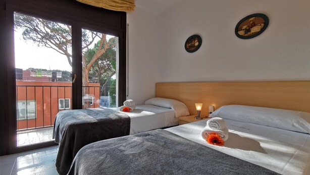 A hotel room with two beds, a balcony, and a view of trees and buildings. - Beachside Apartment with Free WiFi, Terraces & Near Shops and Restaurants (Platja d'Aro)
