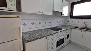 A kitchen with white cabinets, a granite countertop, a built-in oven, a washing machine, and a window above the sink. - Beachside Apartment with Free WiFi, Terraces & Near Shops and Restaurants (Platja d'Aro)