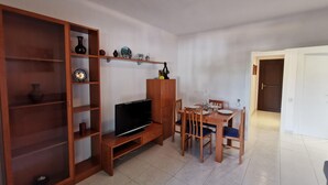A living room with a TV, wooden cabinet, and dining table with chairs. - Beachside Apartment with Free WiFi, Terraces & Near Shops and Restaurants (Platja d'Aro)