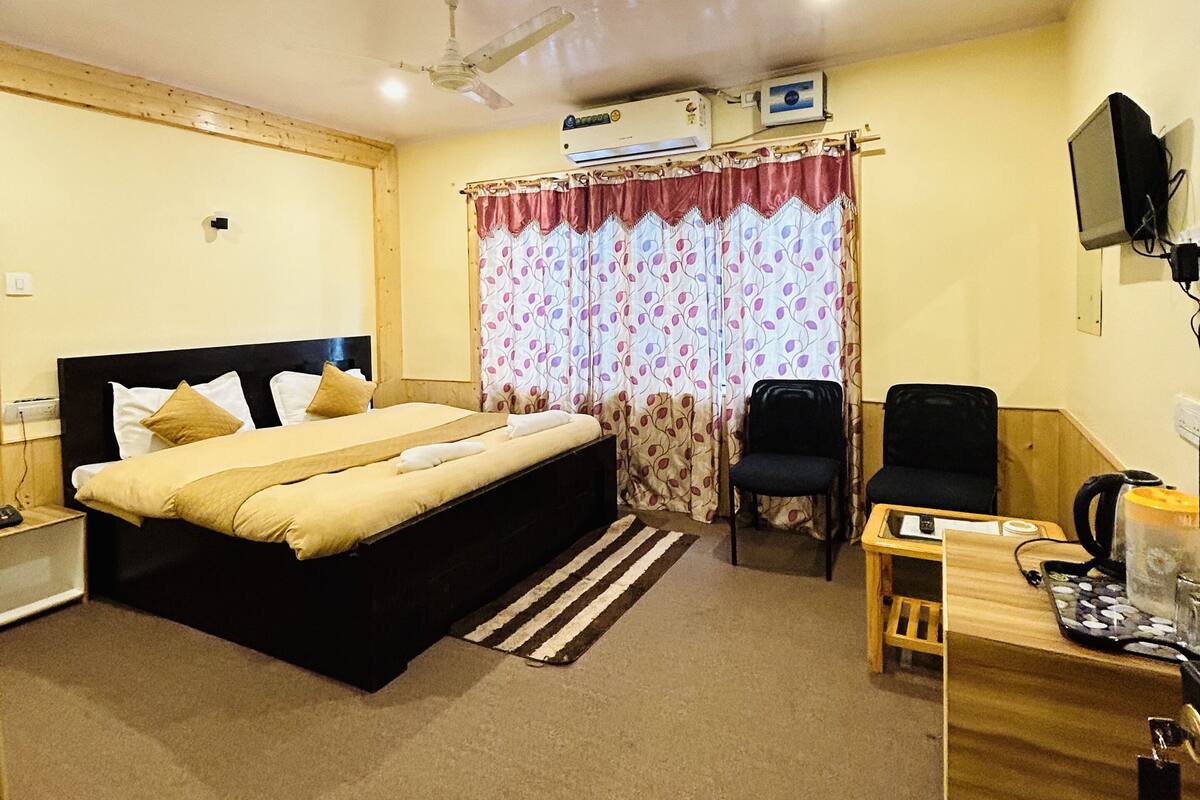A bedroom with a bed, a desk, a chair, a ceiling fan, and an air conditioning unit.