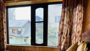 A bedroom with a large window, wooden walls, and a bed with multiple pillows. - The Iceland Hotel Srinagar (Srinagar)