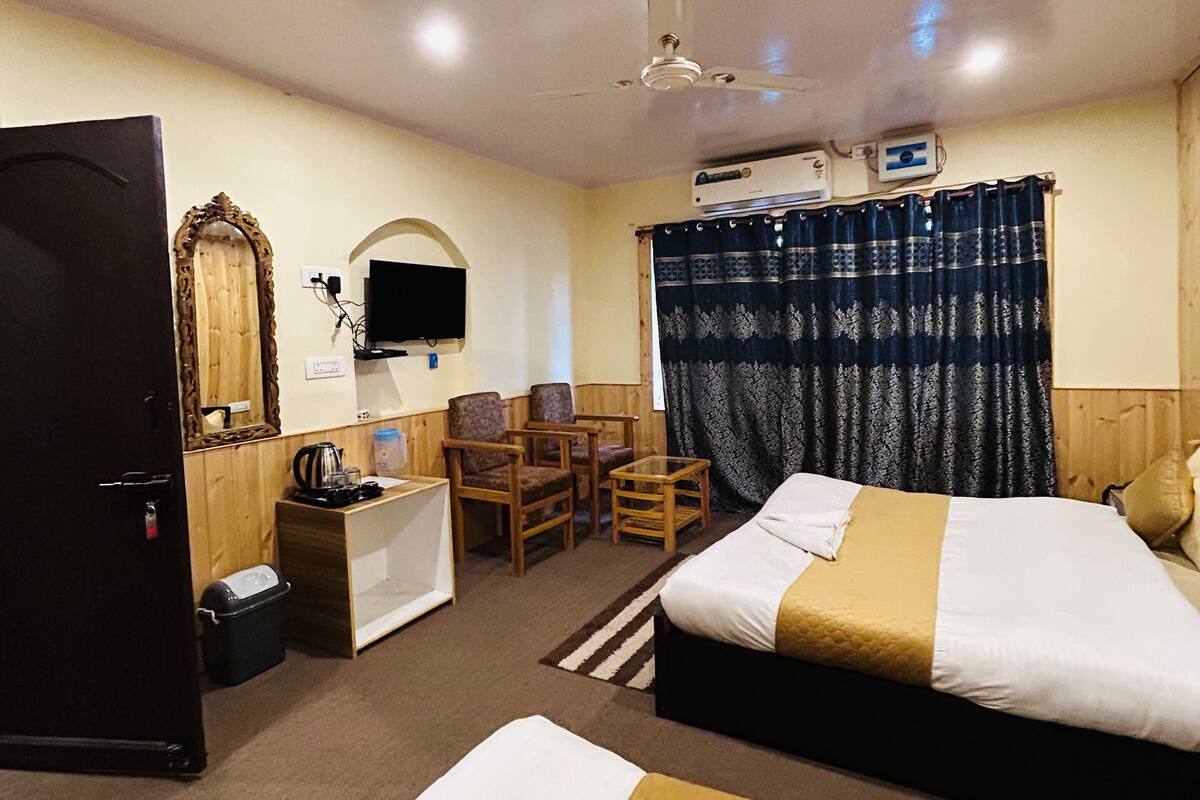 A hotel room with two beds, a desk, a chair, a television, and a ceiling fan.