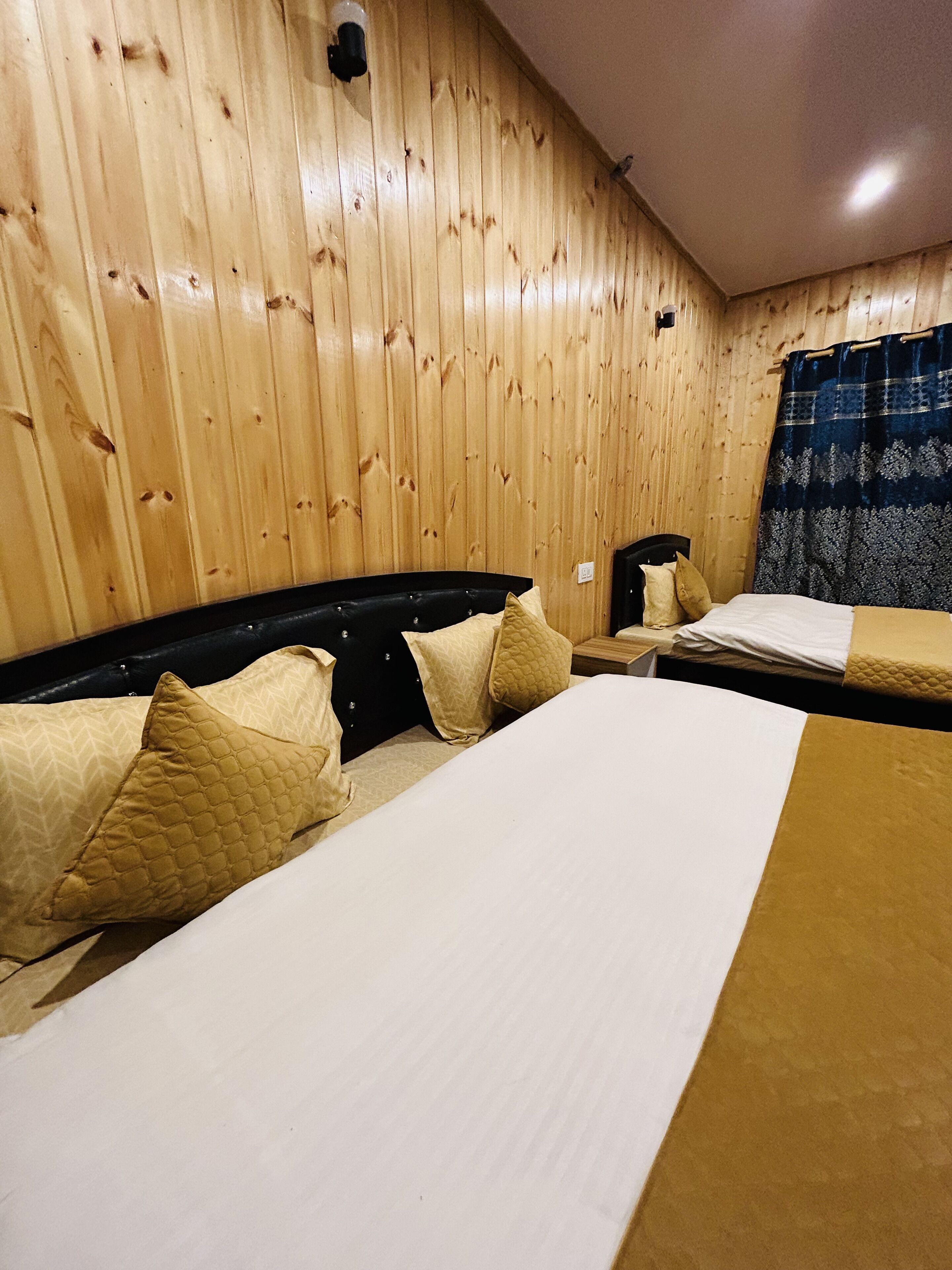 A room with wooden panel walls, two beds with white and brown bedding, and a dark headboard.